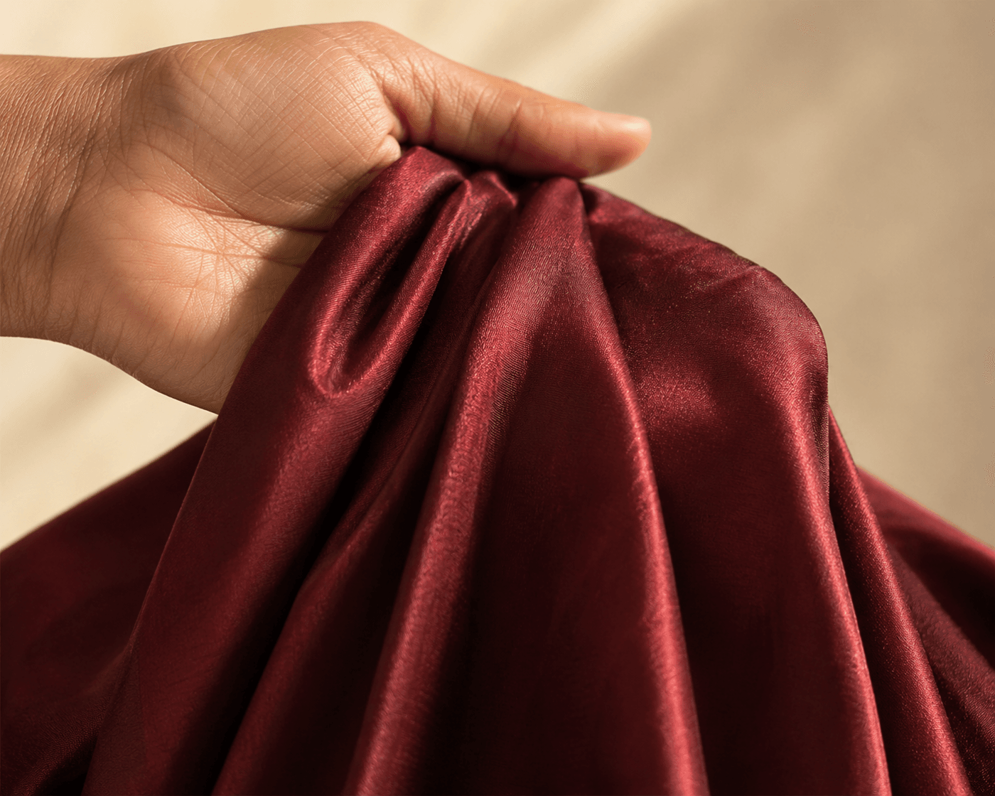 Woman's hand holding pure silk saree fabric to test weight and drape — the silk pools naturally in the palm with characteristic luster and weight.