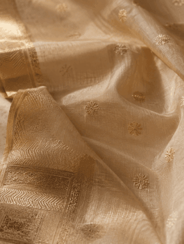 Pale gold Chanderi silk-cotton saree with zari border and floral butti motifs on white marble