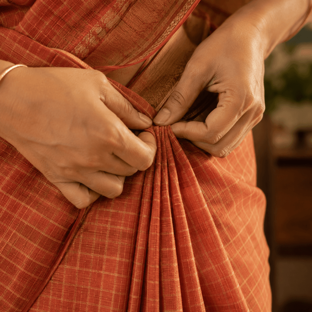 Close-up of hands pleating a saree into even folds at the waist