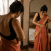 Woman draping a Nivi-style saree in front of a mirror, tucking pleats at the waist