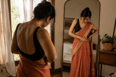 Woman draping a Nivi-style saree in front of a mirror, tucking pleats at the waist