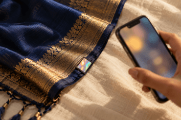 Hand holding a phone beside a hologram label on a silk saree pallu, ready to verify a Silk Mark
