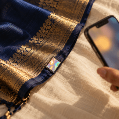 Hand holding a phone beside a hologram label on a silk saree pallu, ready to verify a Silk Mark